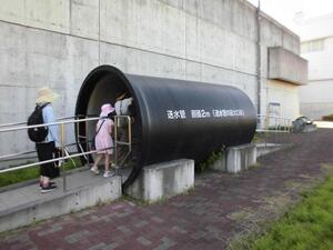 直径2メートルの水道水を送るための送水管の模型の中をくぐってみる参加者の様子